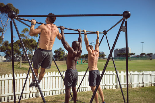 Diverse group of fit shirtless men exercising outdoors, doing pull ups on exercise frame