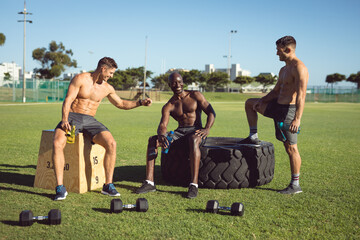 Diverse group of happy shirtless men exercising outdoors, taking a break talking and fist