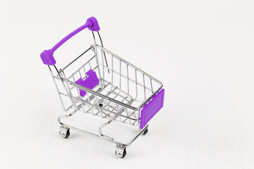 empty metal shiny grocery cart on wheels on white wooden table background