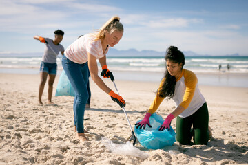 Diverse group of women walking along beach, picking up rubbish