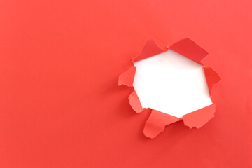 Close up of hole torn in red paper background.