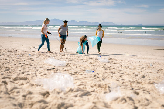 Diverse group of women walking along beach, picking up rubbish