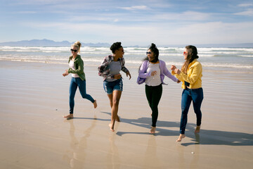 Happy group of diverse female friends having fun, walking along beach and laughing