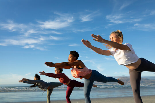 Group of diverse female friends practicing yoga, stretching at the beach