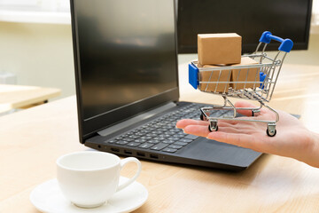 metal chrome cart with boxes on the background of a black laptop and a coffee cup on the table. female hands in the frame. selective focus
