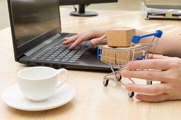 metal chrome cart with boxes on the background of a black laptop and a coffee cup on the table. female hands in the frame. selective focus