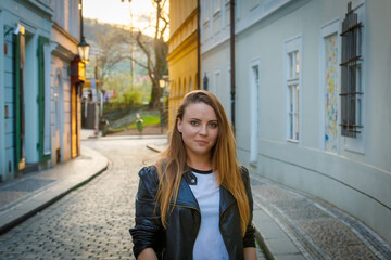 A young girl with long hair is walking along the city street. The road is paved with cobblestones.