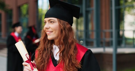 School graduate in academic dress and hat looking at the camera with happy smile. Adorable girl...