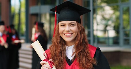 School graduate in academic dress and hat looking at the camera with happy smile. Adorable girl...