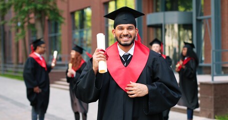 School graduate man in academic gown and hat looking at the camera with happy smile. Happy...