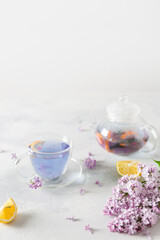 Obraz na płótnie Canvas Spring composition with a cup of purple tea, teapot and lilac flowers on light background. Spring tea party, tea drinking. Menu, greeting card. Copy space