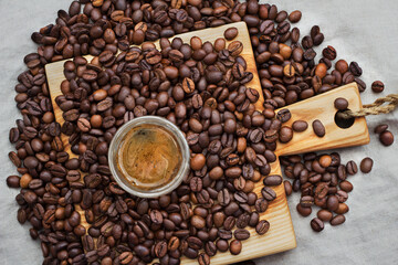 Small glass shot of coffee among selected and calibrated Arabica coffee beans scattered on a napkin, table, blended, top view