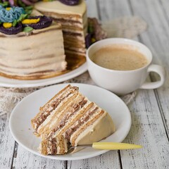 Honey cake on a white table with cup of coffe. Cake with cream flowers. Close up, copy space.