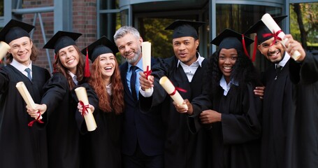 Company of happy multiracial student people are celebrating their graduation while standing near...