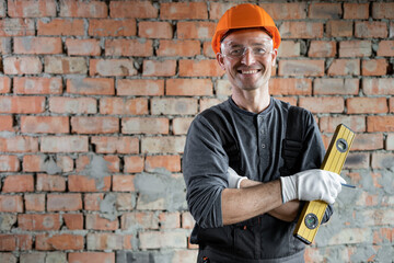 Portrait of a smiling professional repairman standing near the wall with a building level in his...