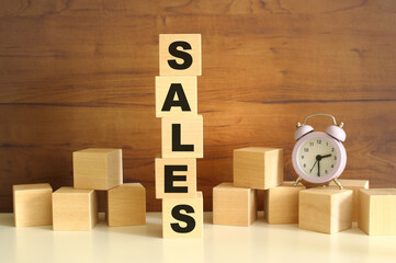 Five wooden cubes stacked vertically on a brown background make up the word SALES.