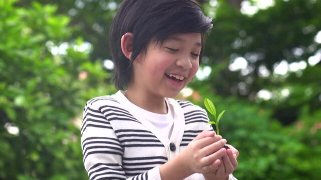 Happy Asian Child Holding Young Plant In Hands With Nature Background