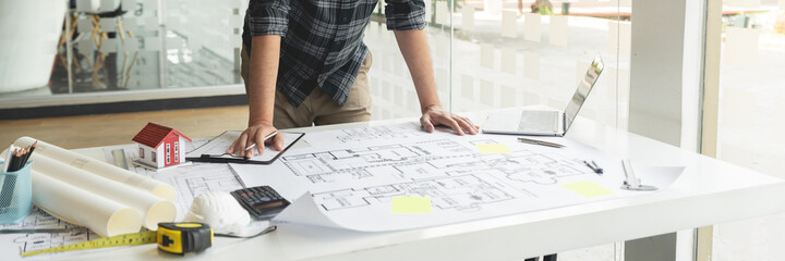 A hand holding a pencil sketching and designing a large and complex blueprint