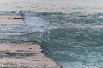 Blue sea wave rolls water on concrete pier. Sea morning landscape clear transparent wave close up. Pink reflection and glitter on pier from gentle dawn sky.
