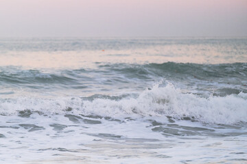 Naklejka premium Minimalist seascape. Blue clear sea water and white foam from waves against background of horizon and bright delicate pink dawn sky in the morning.
