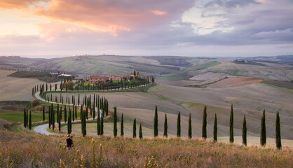 young girl takes a photo of farm and road with cypress at sunset in Val d'Orcia. Tuscany. Italy
