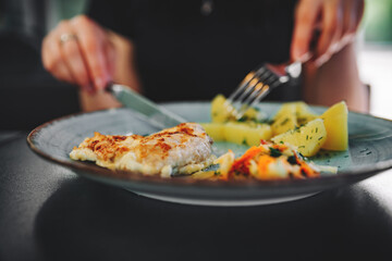 woman hand holding fork and knife eat chicken breast meat with potato in a plate