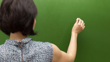 A female teacher writes with chalk on a blackboard close up.