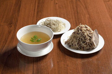 Asian cuisine Uzbek food Naryn, sliced boiled dough noodles with finely chopped meat on a plate with horse meat sausage and a plate of beef broth and a plate of onions on the table