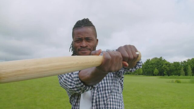 Closeup portrait of stylish attractive african american male hitter with dreadlocks swinging baseball bat, preparing for pitch, looking with concentrated expression while playing baseball outdoors.