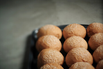 a part of oven tray full with sesame burger buns put on rusty kitchen table with copyspace by narrow focusing  only on one bread with tilt-shift lens effect that made other soft and blurred