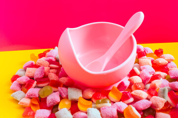 Children's tableware silicone bowl with spoon. Serving baby food, kid dishware.Pink silicone bowl and spoon are in a heap of sweets and marmalade. bright, colorful photo