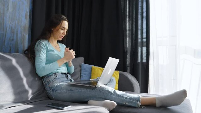 Cheerful woman in casual wear having video call on laptop while sitting on sofa at home, gesturing and talking emotionally. Arc shot business coach giving consultation. Online meeting