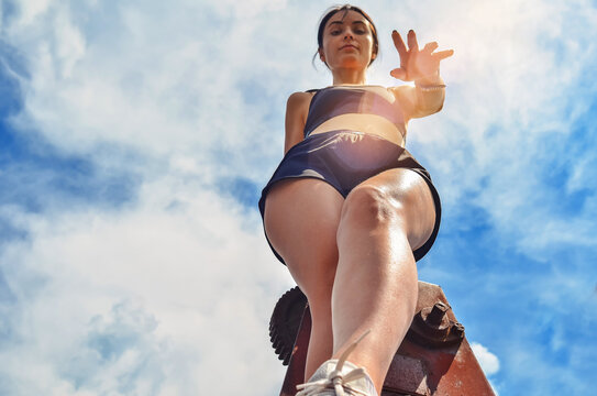 Athletic Girl In Black Sports Shorts And A Top Stands On A Background Of Sky View From Below