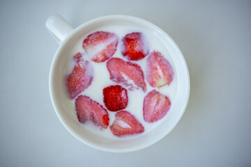 halves of strawberries floating in a cup with milk on a white background