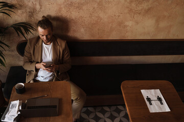 Fototapeta na wymiar Young white man using mobile phone while working with laptop in cafe