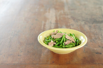 Fried beans with pork in a yellow bowl on the dining table
