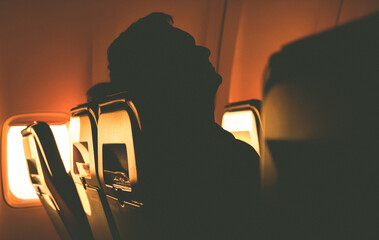 sleeping tourist silhouette in airplane chair at sunrise from porthole 