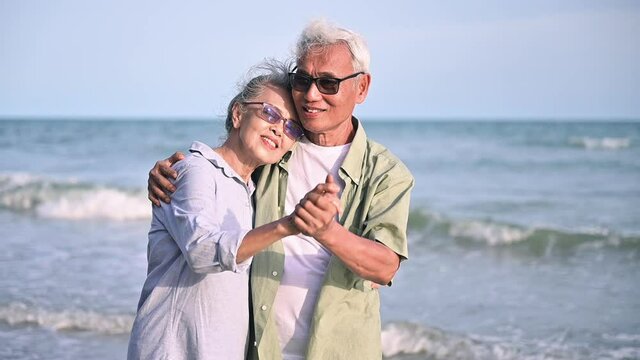 Asian Senior Couple Tourist Is Hand In Hands, Embrace And Dancing On Tropical Sea Beach In Summer Holiday. Happy Family Couple Elderly Older Retire Resting Relax Together Lifestyle On Seaside Outdoor.