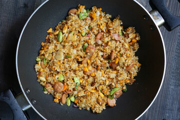 Homemade fried rice with a mixture of eggs, bitter been, and sausage in a frying pan        