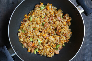 Homemade fried rice with a mixture of eggs, bitter been, and sausage in a frying pan        