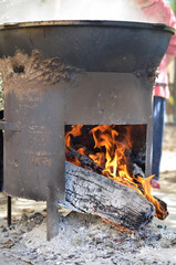 Big black cauldron on the street under it there is a fire burning, a flame of fire and charred logs and ashes
