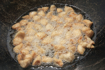 Large chunks of raw lamb fat dumba are fried in oil with bubbles in a black cauldron close-up, cooking food