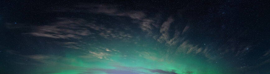 Fototapeta na wymiar Panoramic real photo of beautiful soft Aurora Borealis - bright green lights on black night sky with some clouds. A lot of real stars seen in Northern hemisphere, background picture