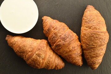 Three delicious croissants with chocolate filling on a slate board with a sour cream saucer, close-up, top view.