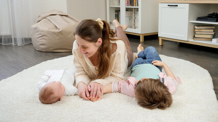 Cute baby and older boy lying with smiling mother on carpet in living room. Parenting, children...