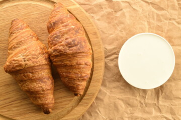 Two delicious croissants with chocolate filling on a round wooden tray with a saucer of sour cream on craft paper, close-up, top view.