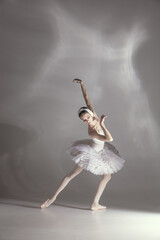 Young graceful balerina in image of white swan in art performance isolated on gray white background.