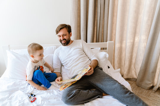 White Father And Son Reading Book While Lying On Bad At Home