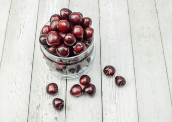 Ripe red cherries in glassware on a light wooden background. Concept of healthy food, diet. Top and side view.