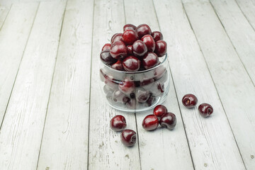 Ripe red cherries in glassware on a light wooden background. Concept of healthy food, diet. Top and side view.